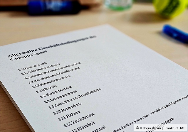 Gestapelte Papierblätter auf einem Tisch; auf dem obersten sind die AGB des CampusSport zu sehen. Im Hintergrund sind Büromaterialien.